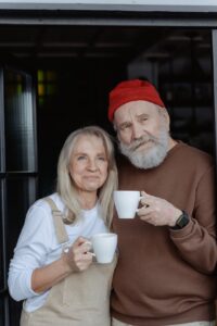 man in brown sweater holding white ceramic mug beside woman in white long sleeve shirt